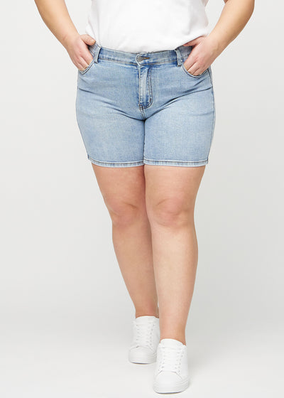 Lys denim skinny short shorts, modelnavn Waves, som sidder tæt til, og slutter midt på låret på en plus-size model, set forfra.