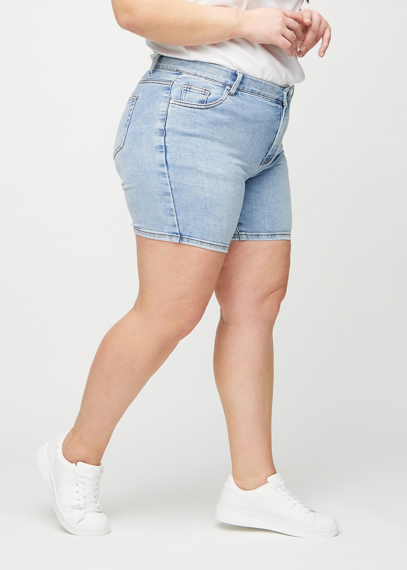 Lys denim skinny short shorts set fra siden på en plus-size model.