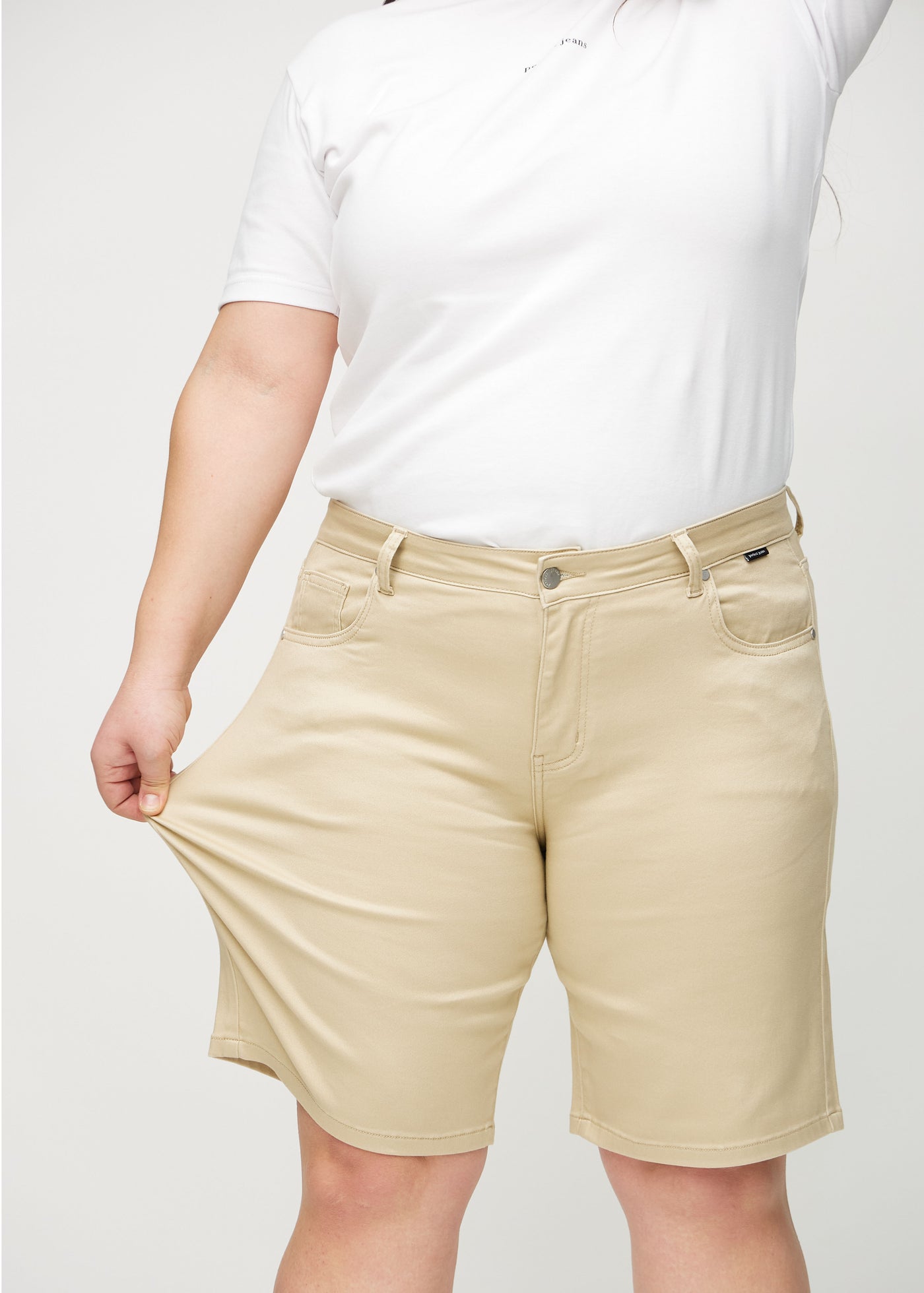 Plus-size model strækker shortsene ved låret for at vise stretch.