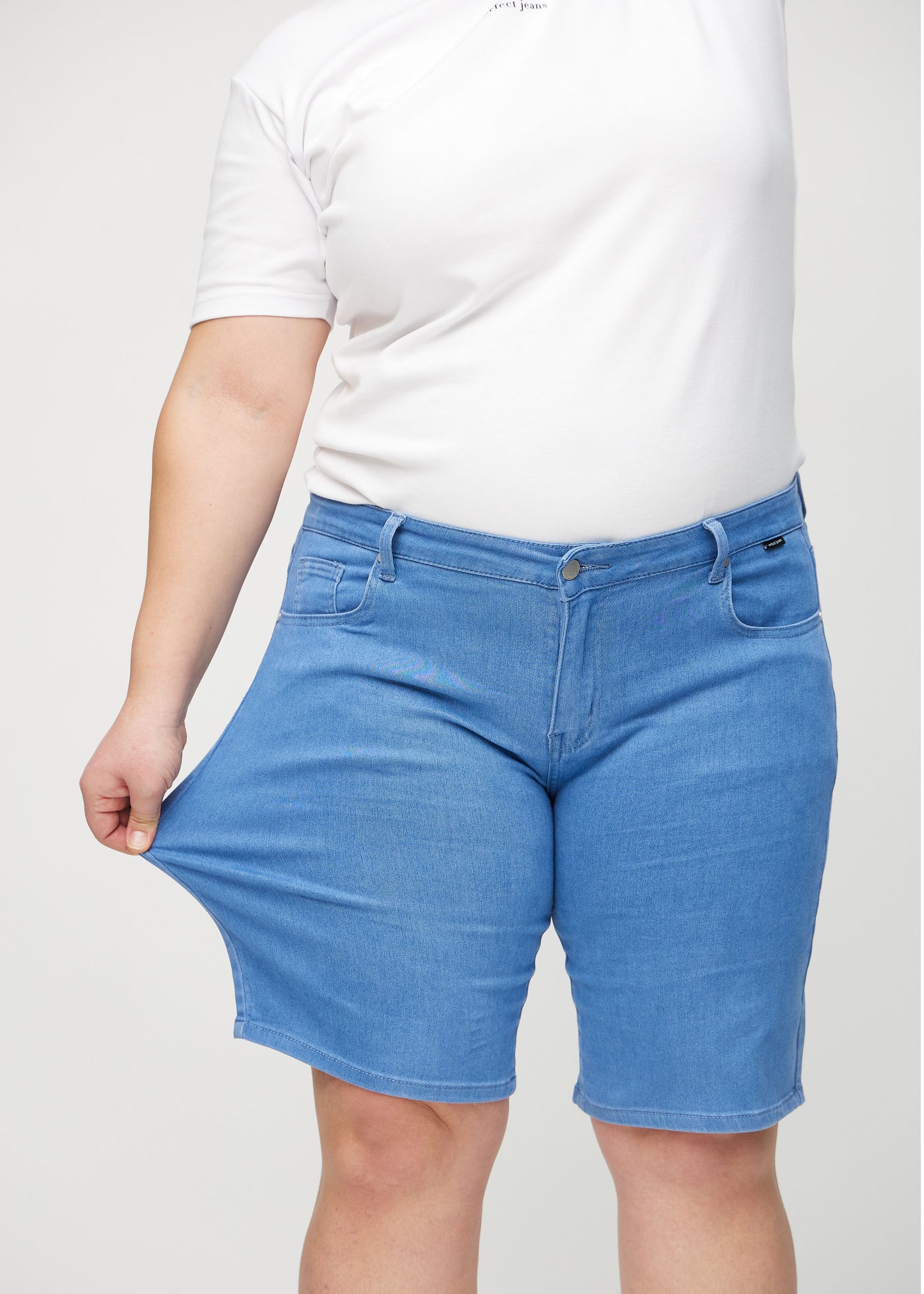 Plus-size model strækker shortsene ved låret for at vise stretch.