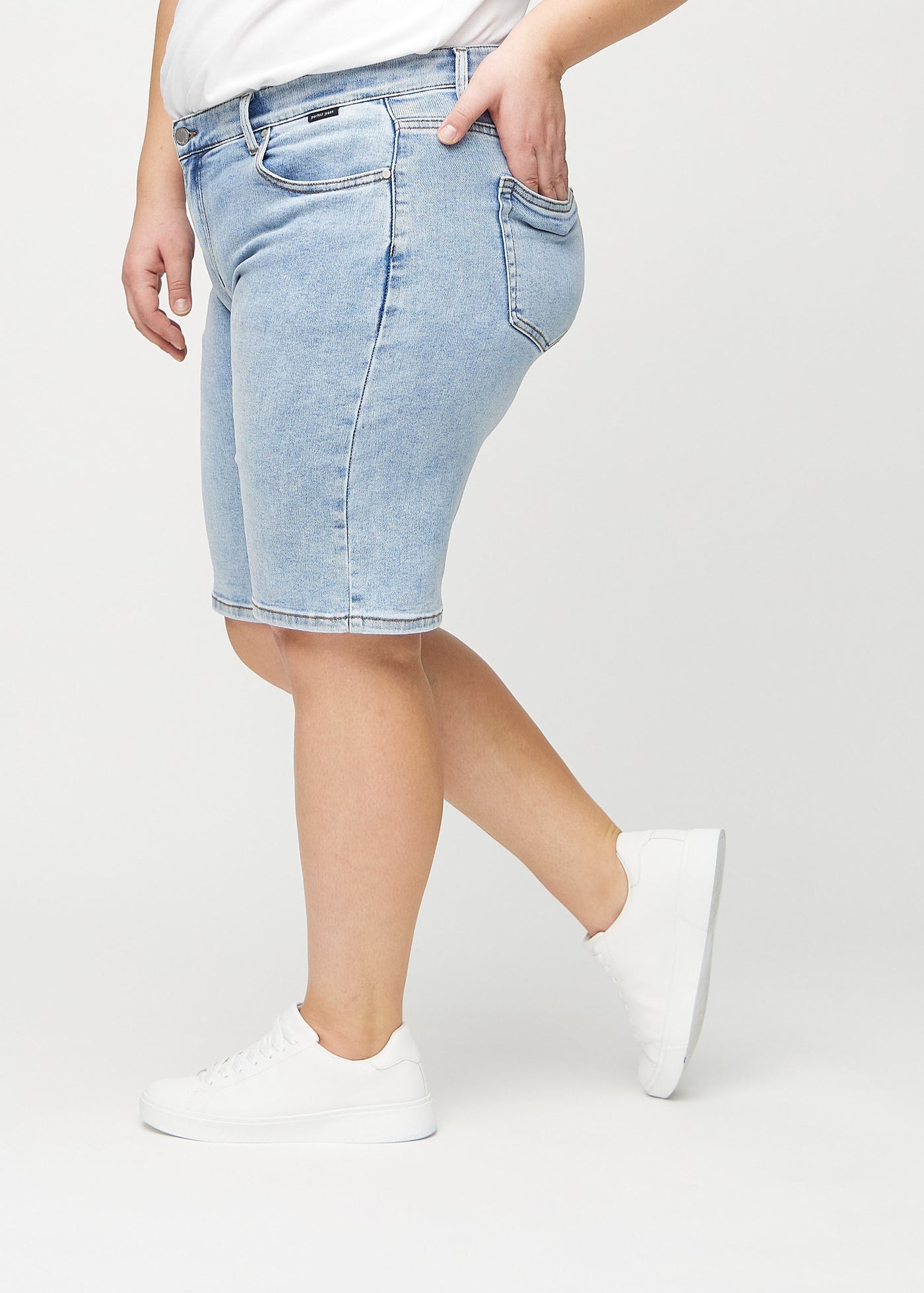 Lys denim regular middle ultra high rise shorts set fra siden på en plus-size model.