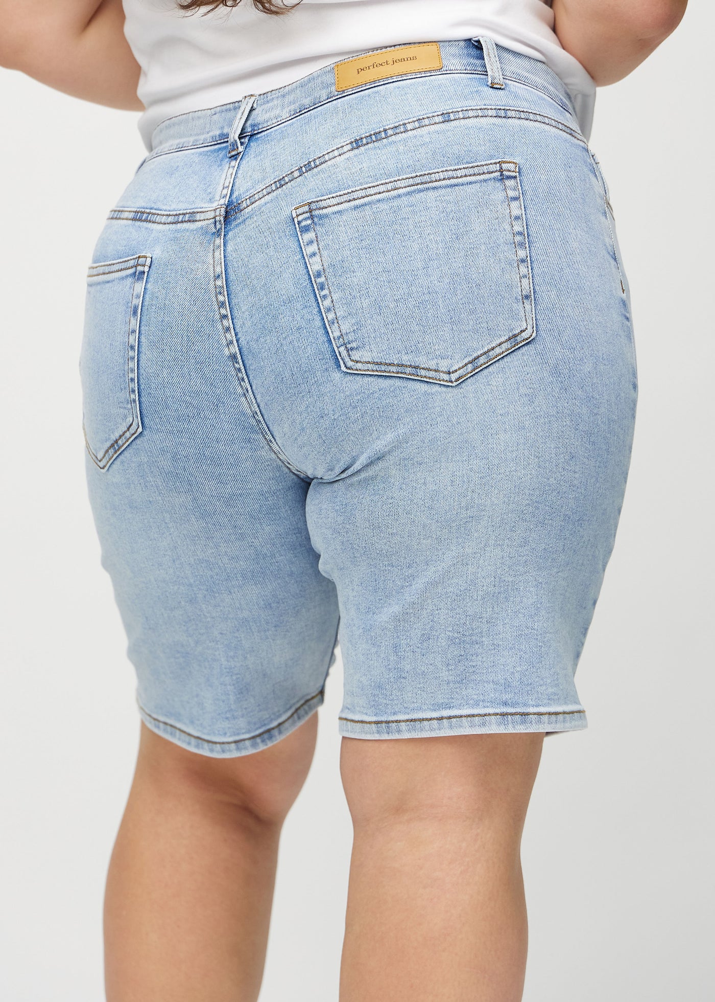 Lys denim regular middle ultra high rise shorts set bagfra tæt på en plus-size model for at vise detaljer.