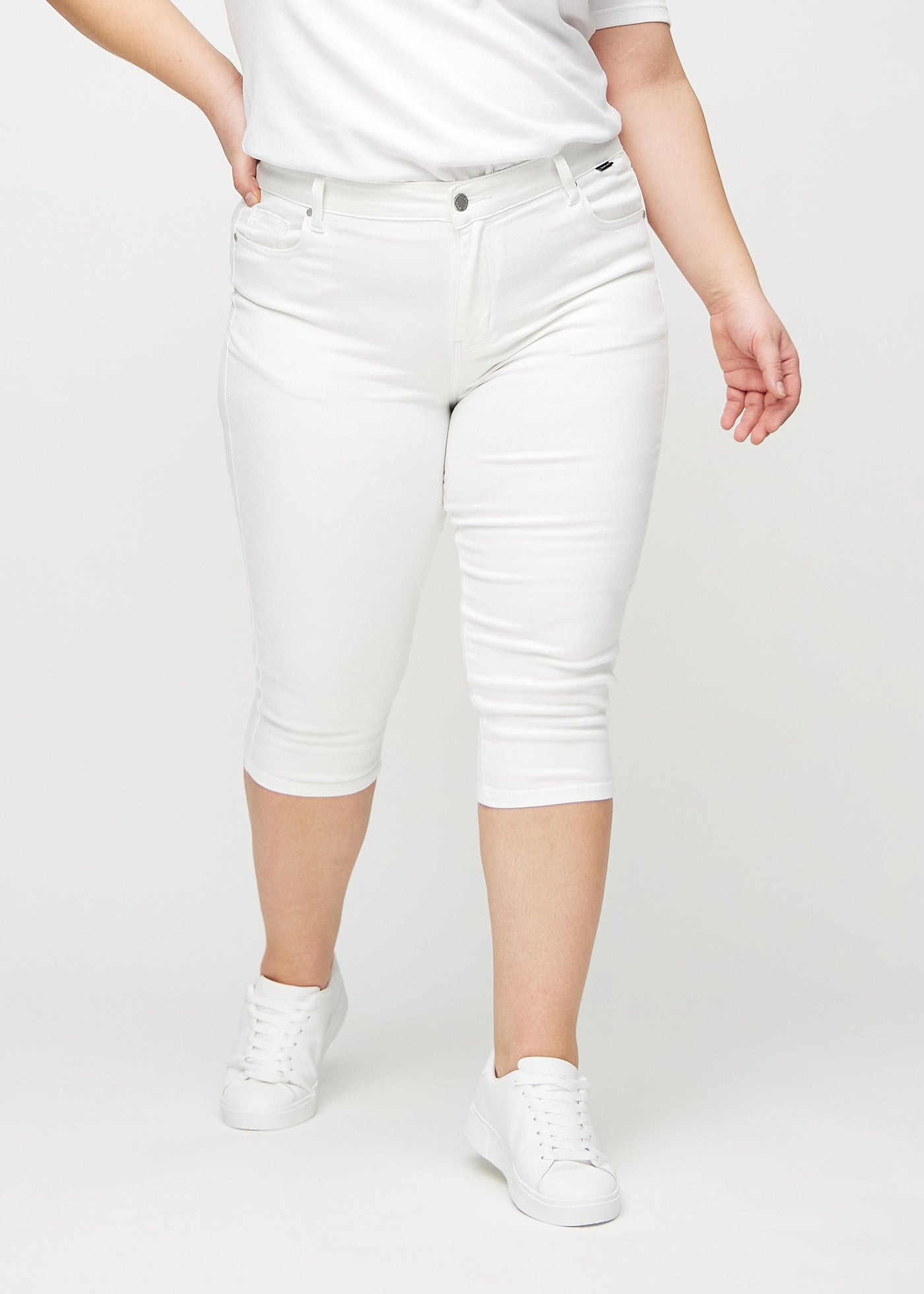 Hvide skinny capris, modelnavn Marguerites, som sidder tæt til benet og slutter lige under knæet på en plus-size model, set forfra.