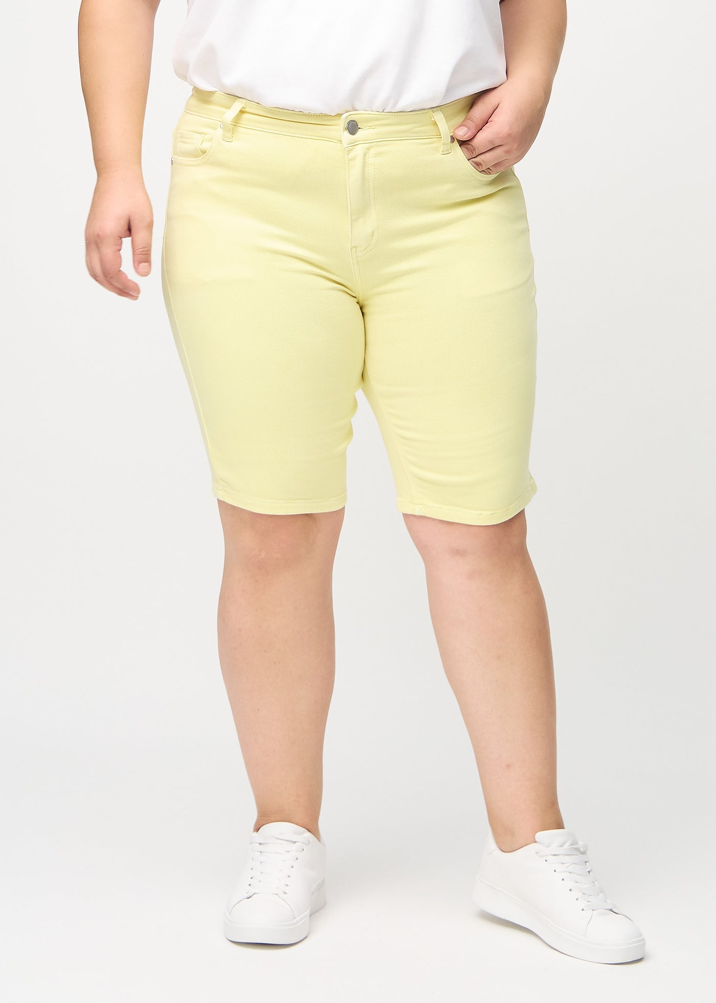 Lysegule skinny middle shorts, modelnavn Lemonades, som sidder tæt til låret og slutter lige over knæet på en plus-size model, set forfra.