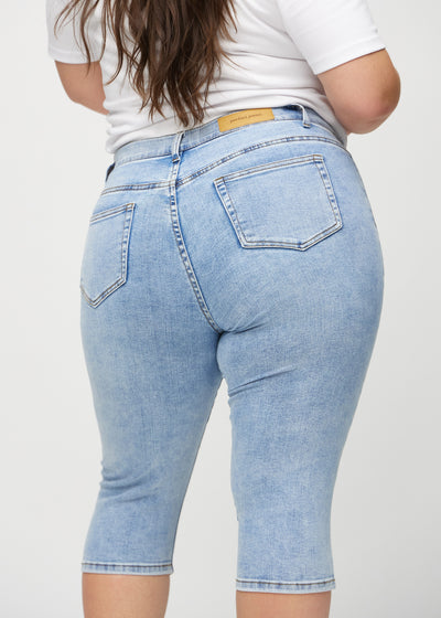 Lys denim skinny capris set bagfra tæt på en plus-size model for at vise detaljer.