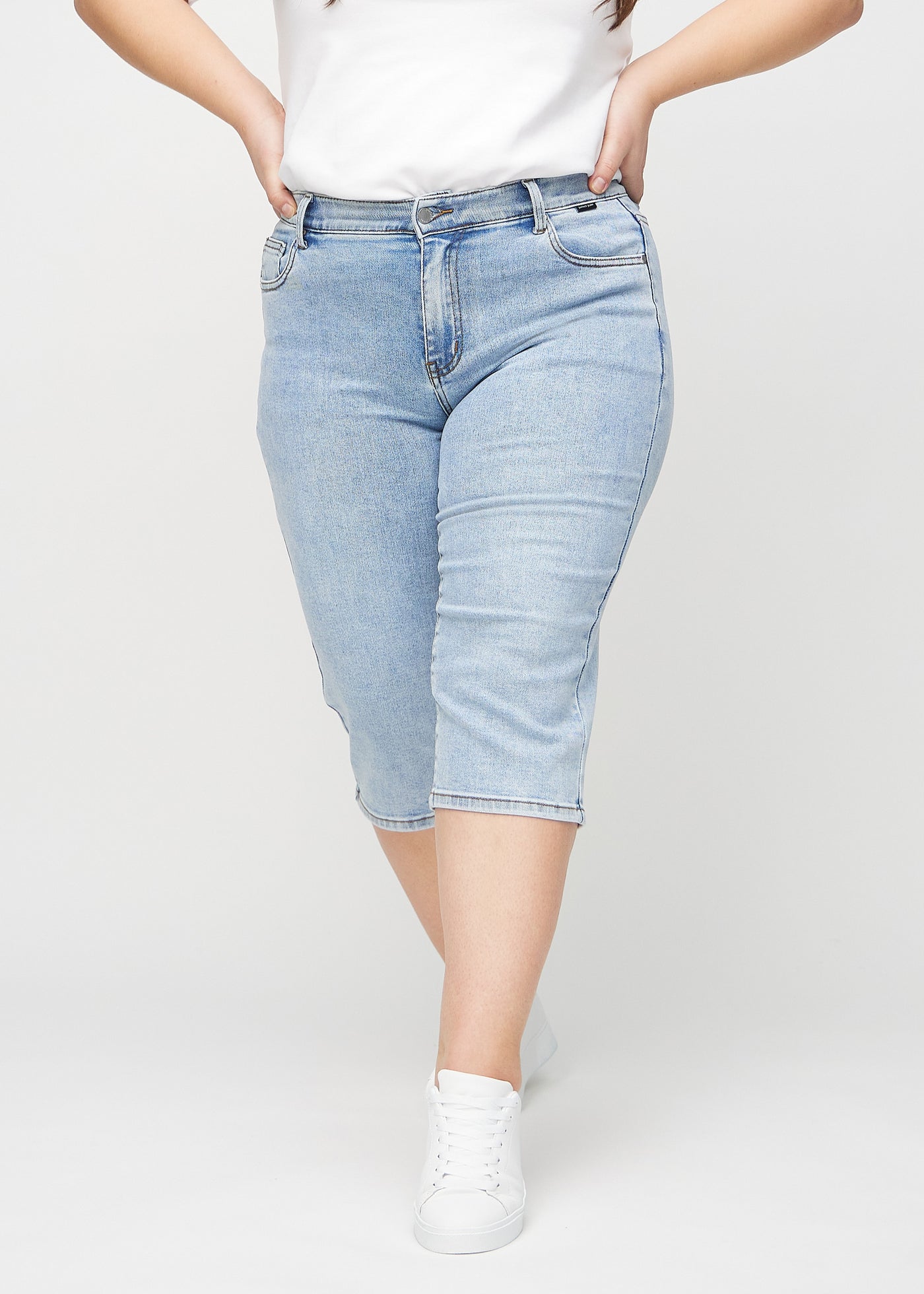 Lys denim regular capris, modelnavn Waves, som sidder lige til benet og slutter lige under knæet på en plus-size model, set forfra.