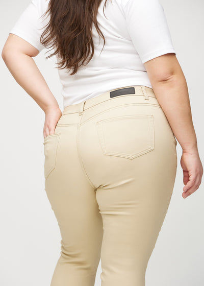 Beige skinny jeans set bagfra tæt på en plus-size model for at vise detaljer.