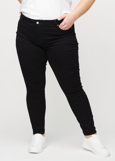 Sorte skinny jeans, modelnavn Ravens, som sidder tæt til benet på en plus-size model, set forfra.