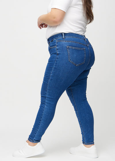 Mørk denim skinny jeans set fra siden på en plus-size model.