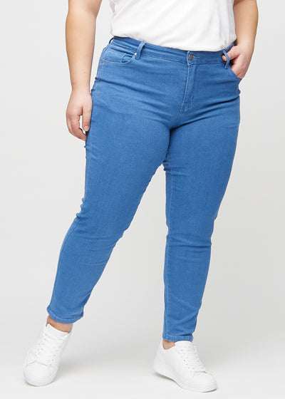 Blå slim jeans, modelnavn Geraniums, som sidder tæt til benet, dog lidt løsere ved anklen, på en plus-size model, set forfra.