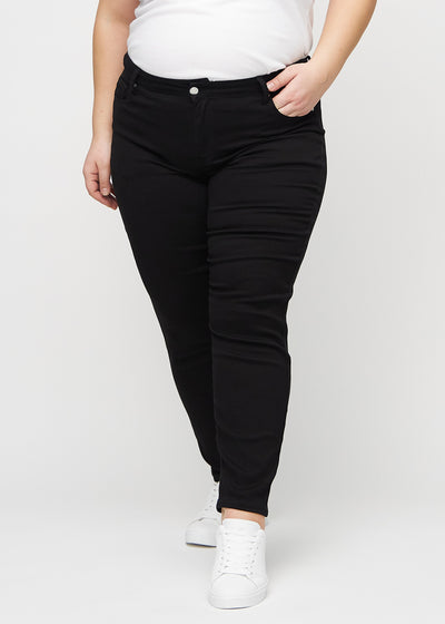 Sorte slim jeans, modelnavn Ravens, som sidder tæt til benet, dog lidt løsere ved anklen, på en plus-size model, set forfra.